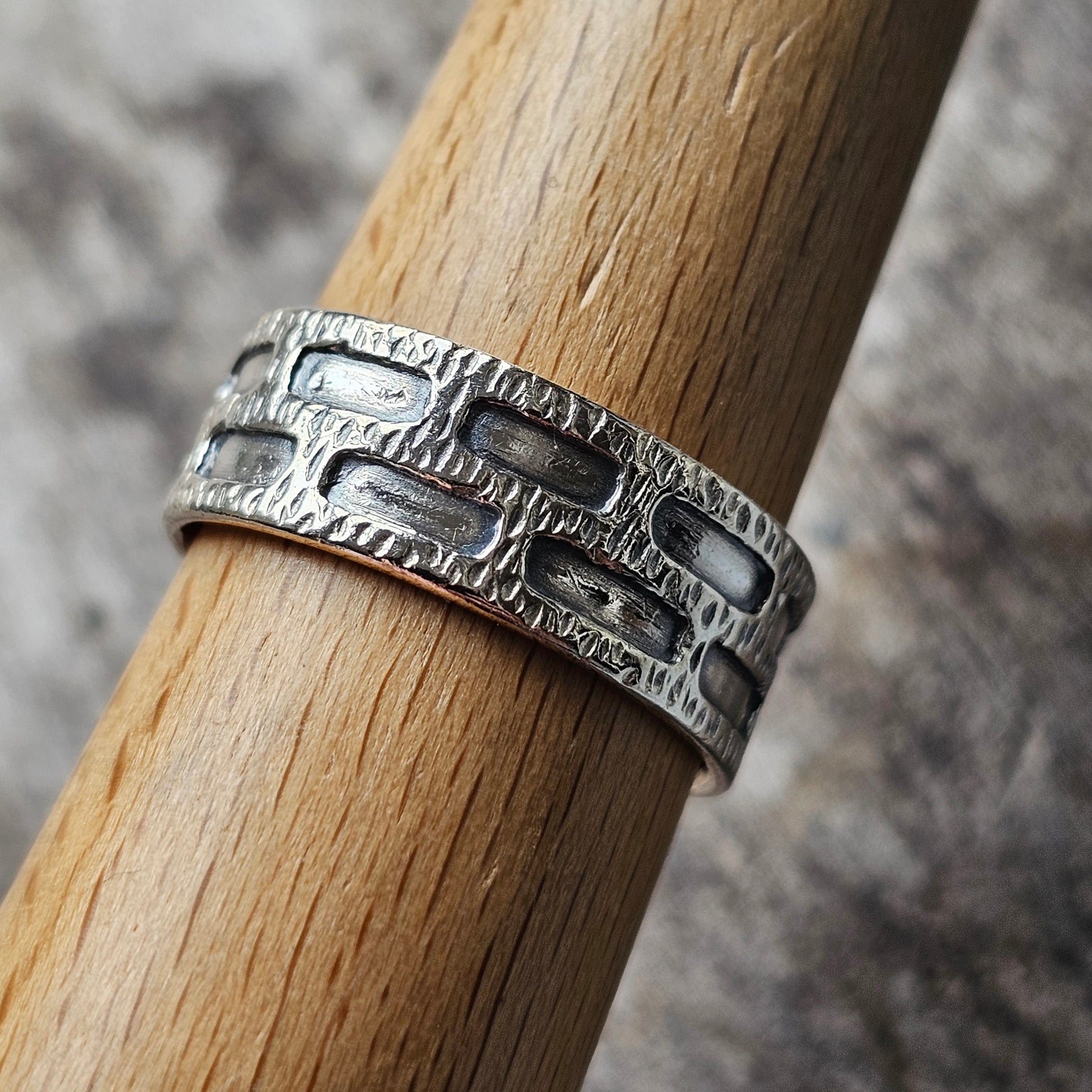 Silver ring with a textured, geometric pattern wrapped around a wooden dowel.