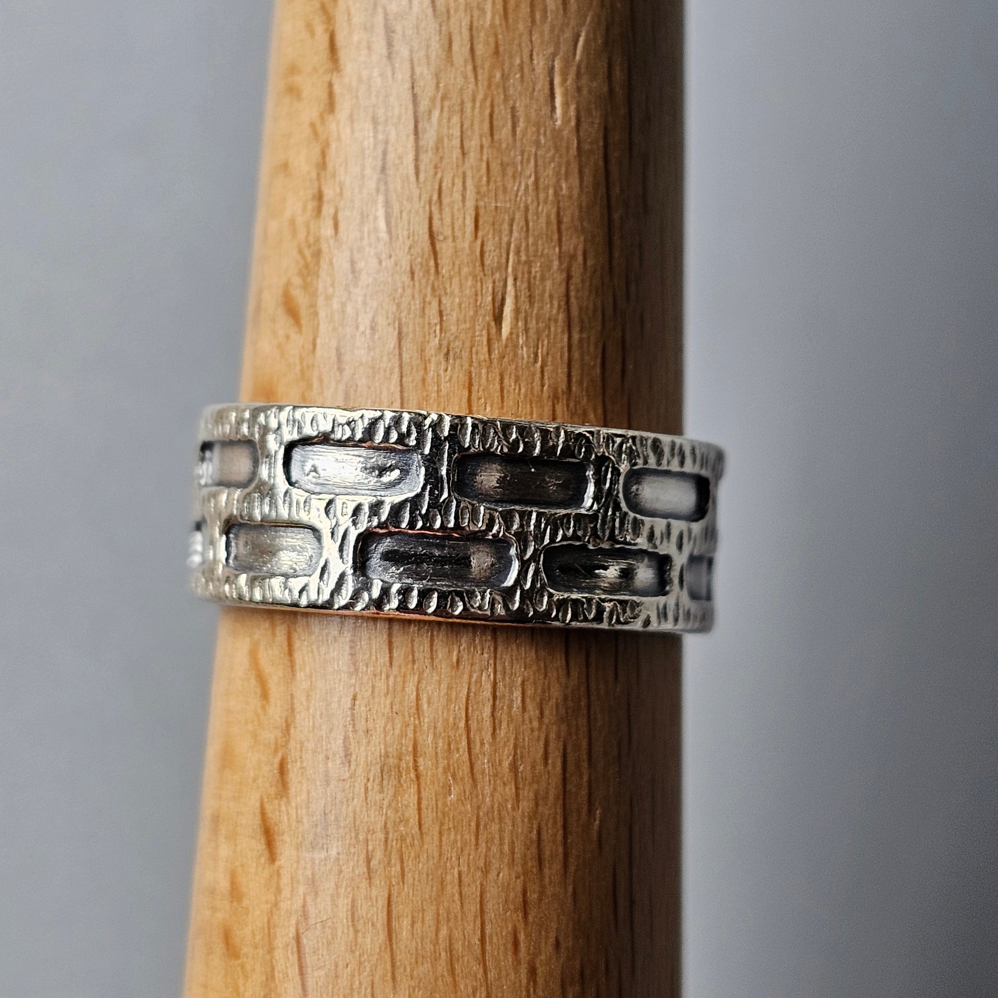 Silver ring with a textured, geometric pattern wrapped around a wooden surface.