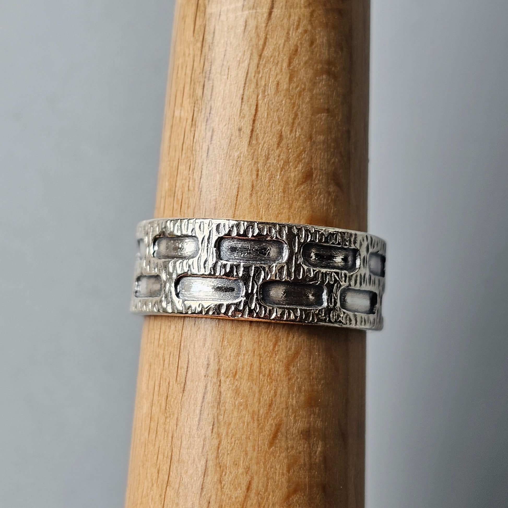 Silver ring with a textured brick-like pattern around its band.