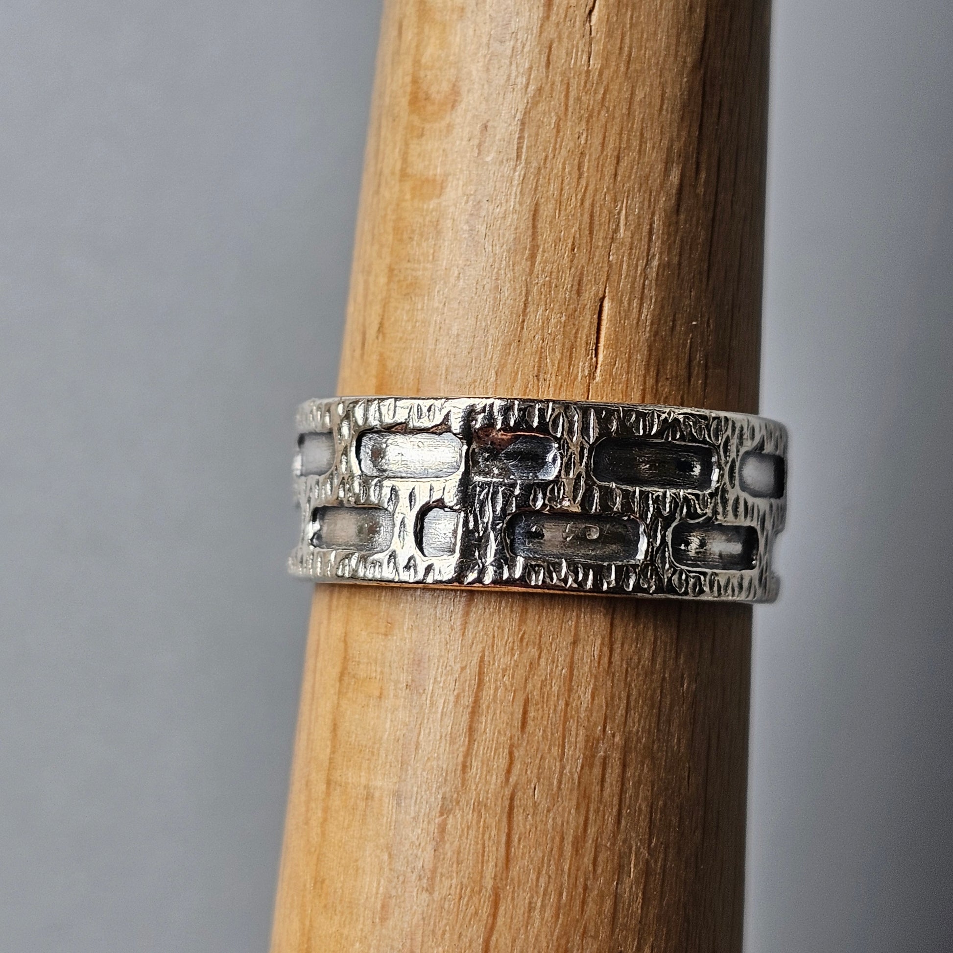 Silver ring with a textured, geometric pattern around its band.