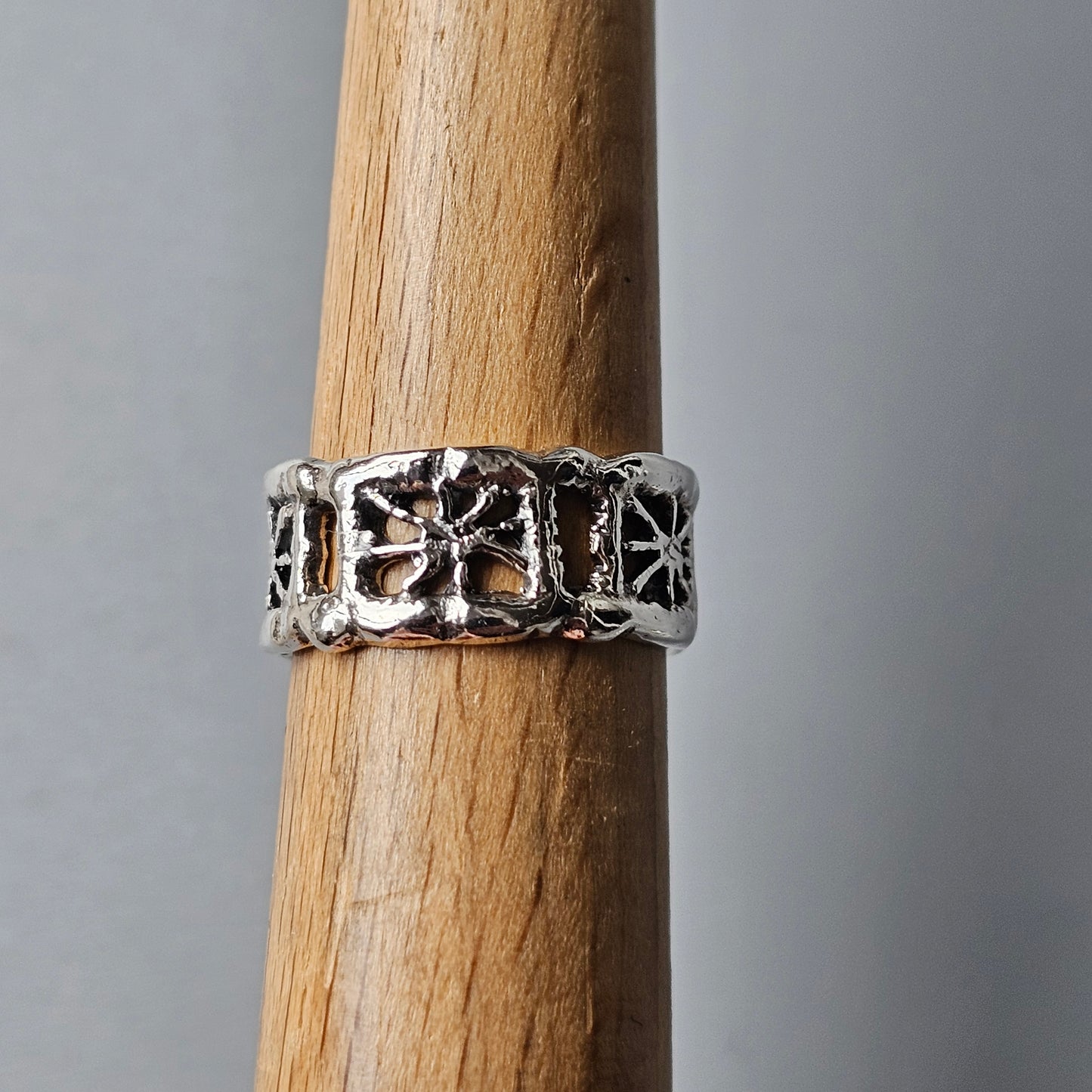 Silver ring with a decorative cross or floral pattern engraved around its band.