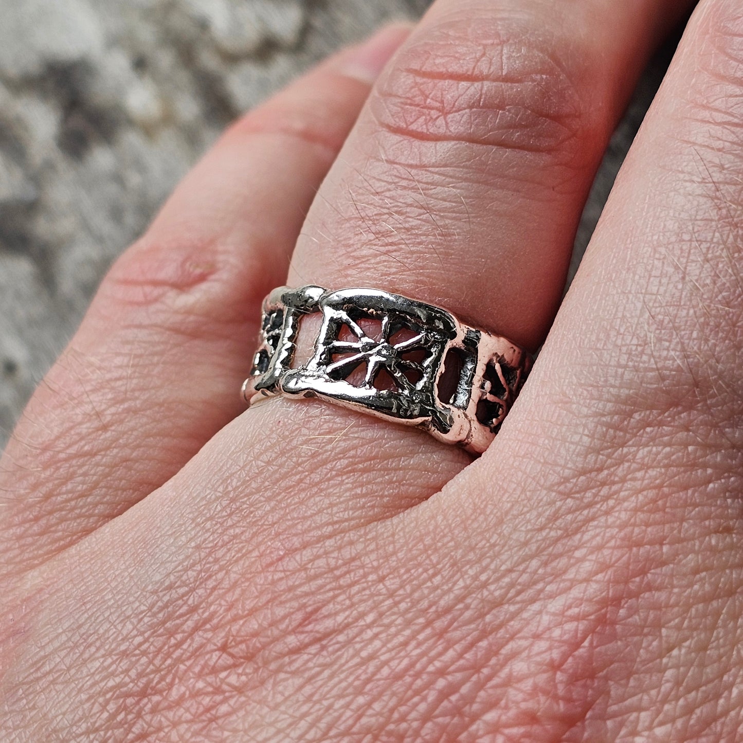 Ornate silver ring with intricate cross and floral designs worn on a finger.