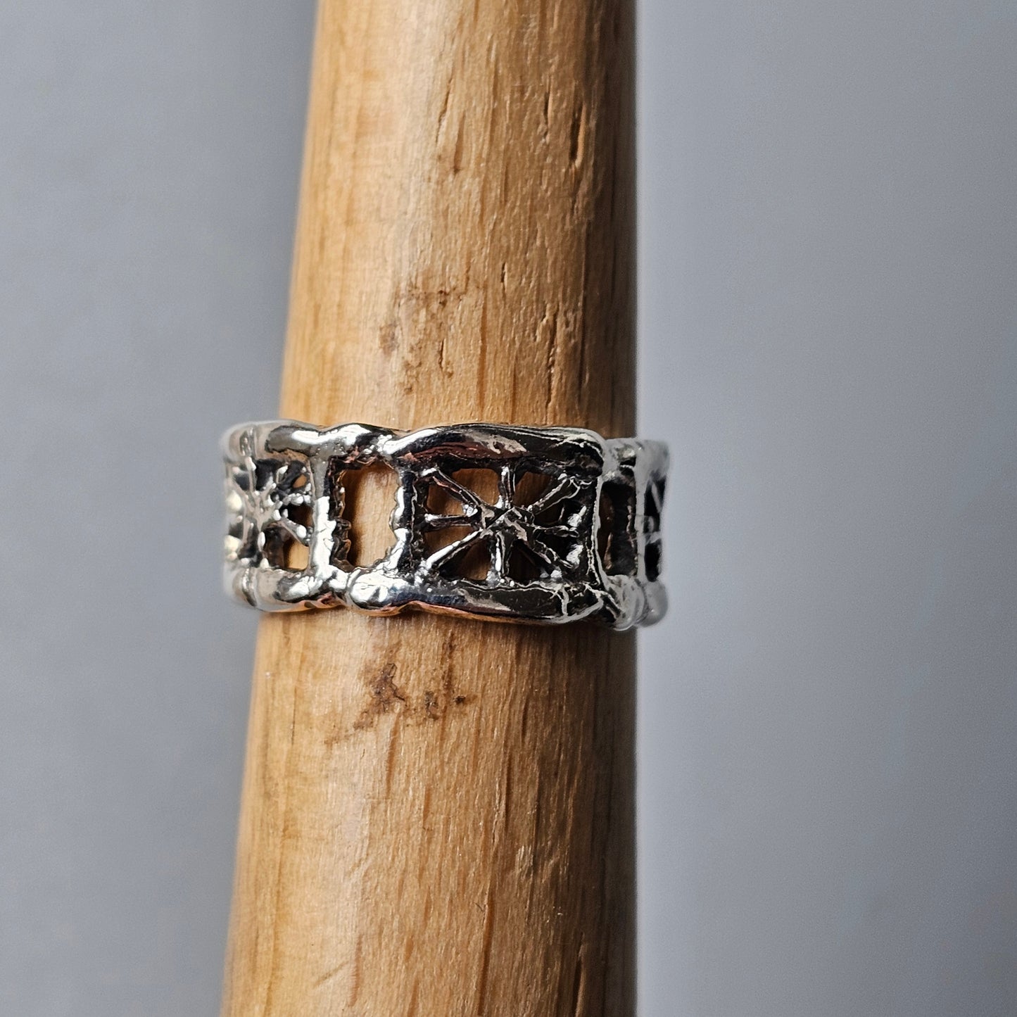 Ornate silver ring with an intricate openwork design displayed on a wooden surface.