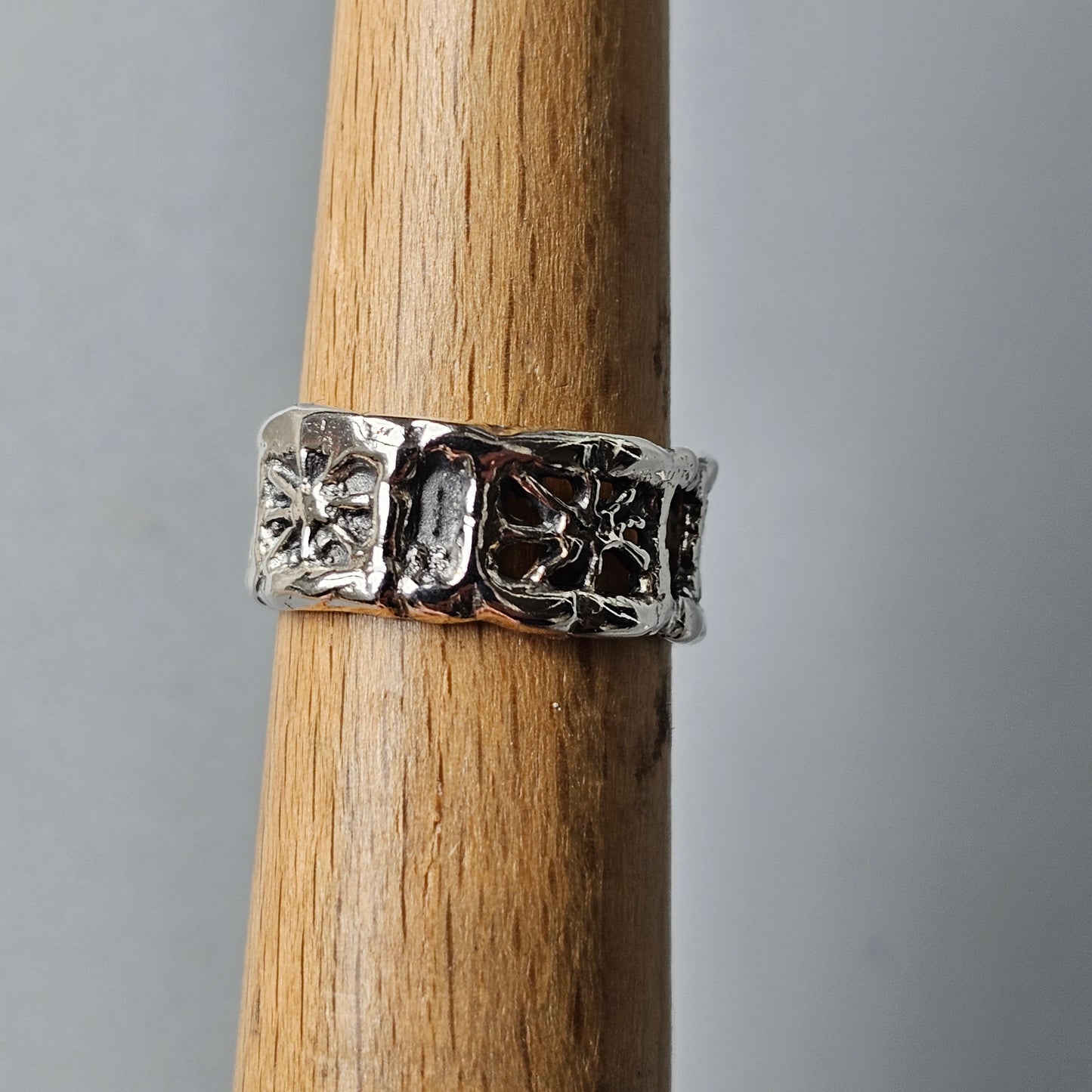 Ornate silver ring with floral or cross-like designs on a wooden surface.