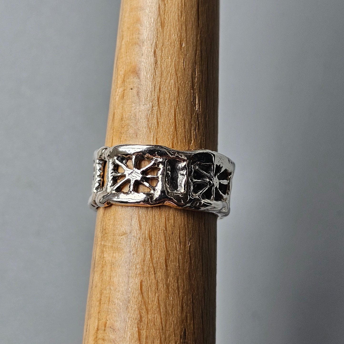 Silver ring with decorative cross or star patterns engraved around the band.