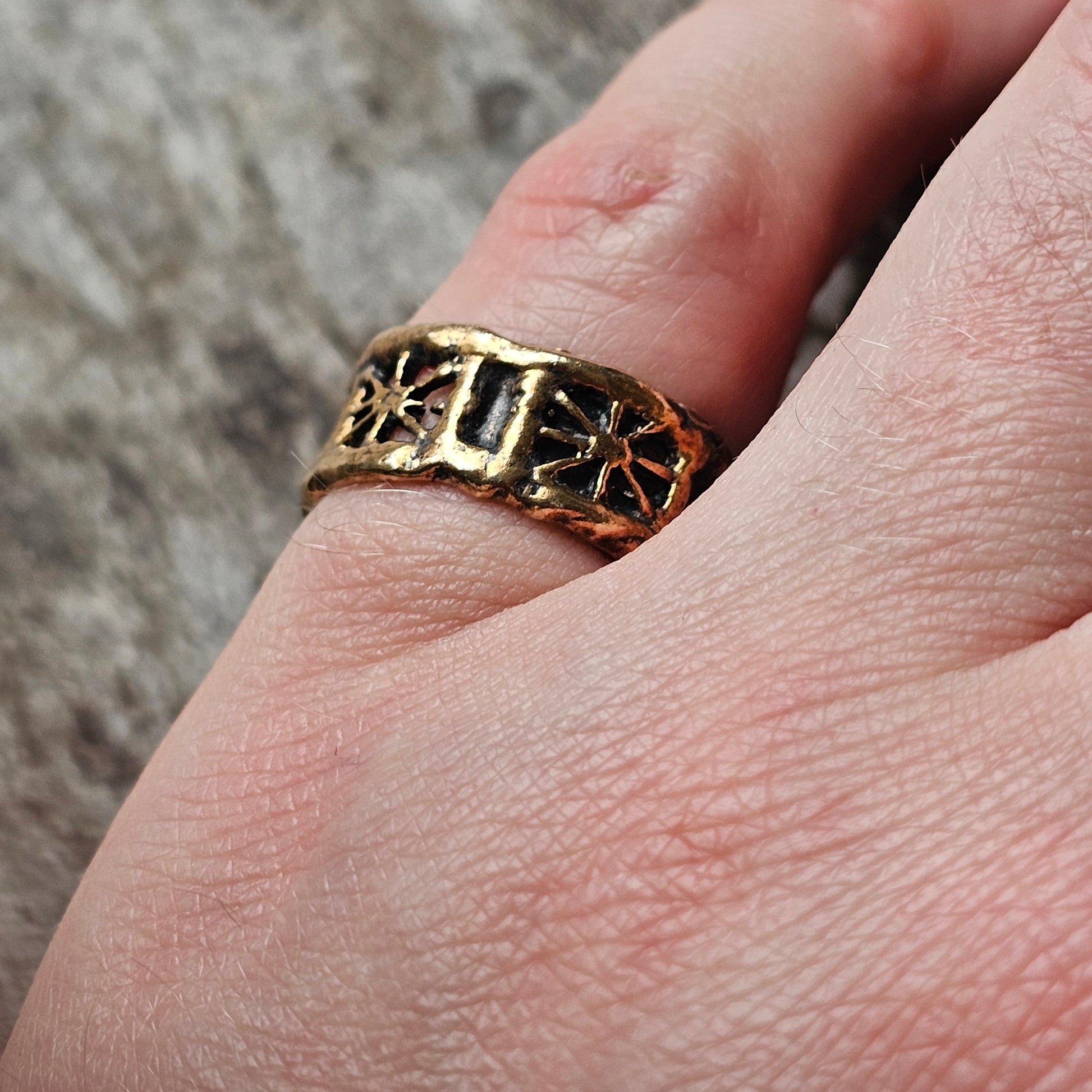 Gold-toned ring with ornate floral or star-like designs worn on a finger.