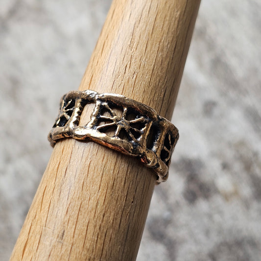 Ornate metal ring with intricate cutout designs worn on a wooden dowel.