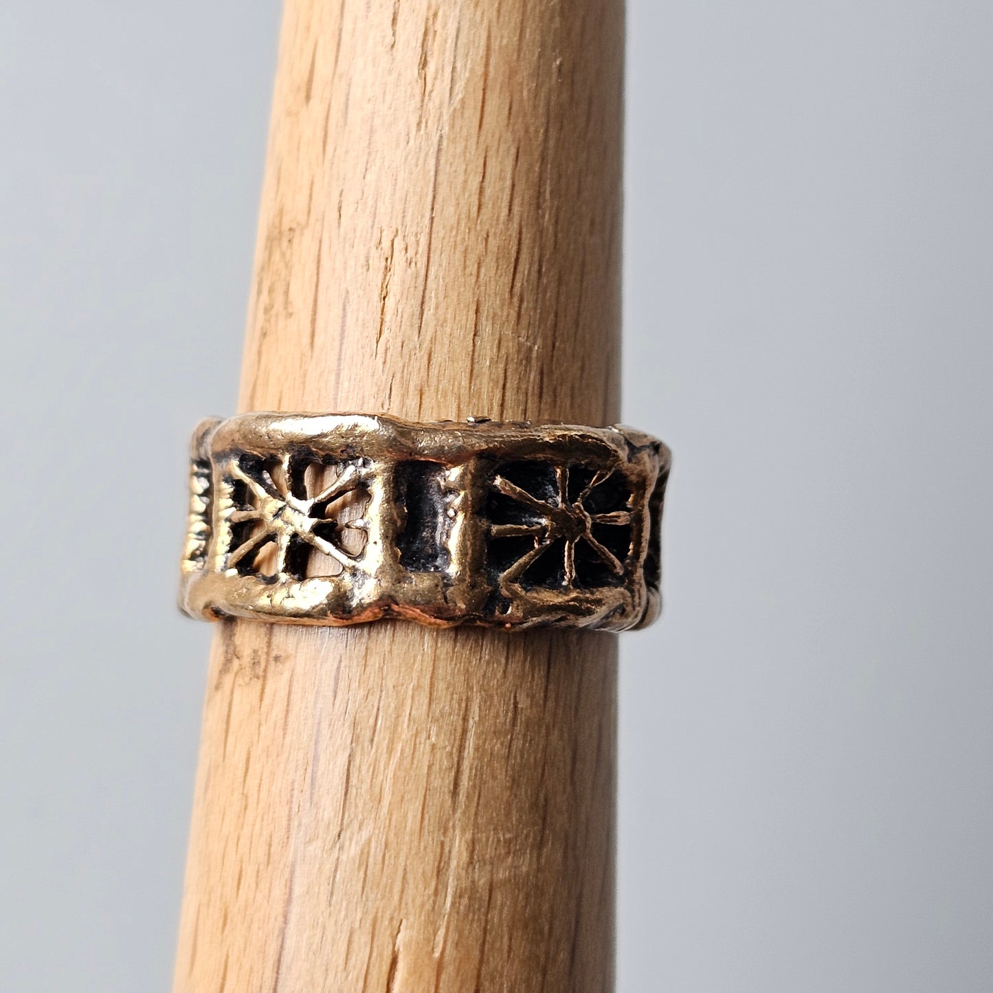 Ornate metal ring with star-like designs worn on a wooden dowel.