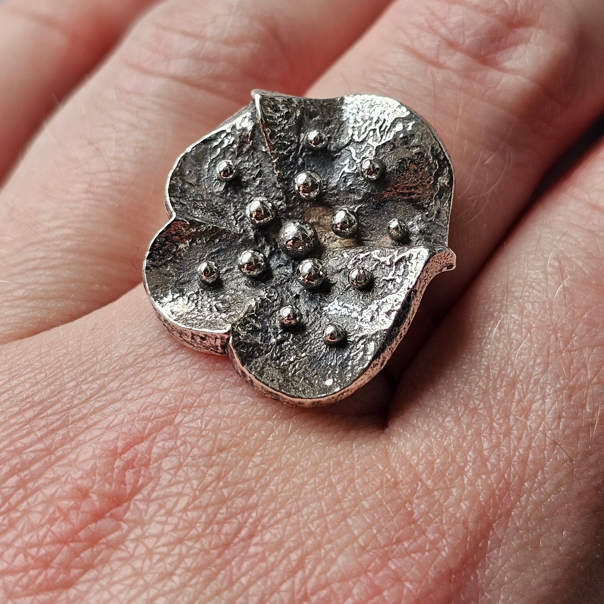 Textured silver ring with a flower-like shape and raised bumps on its surface.