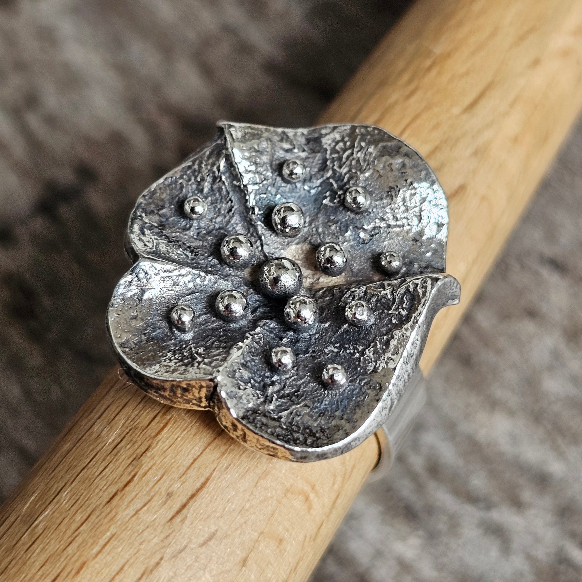 Silver flower-shaped ring with textured petals and raised bead details.