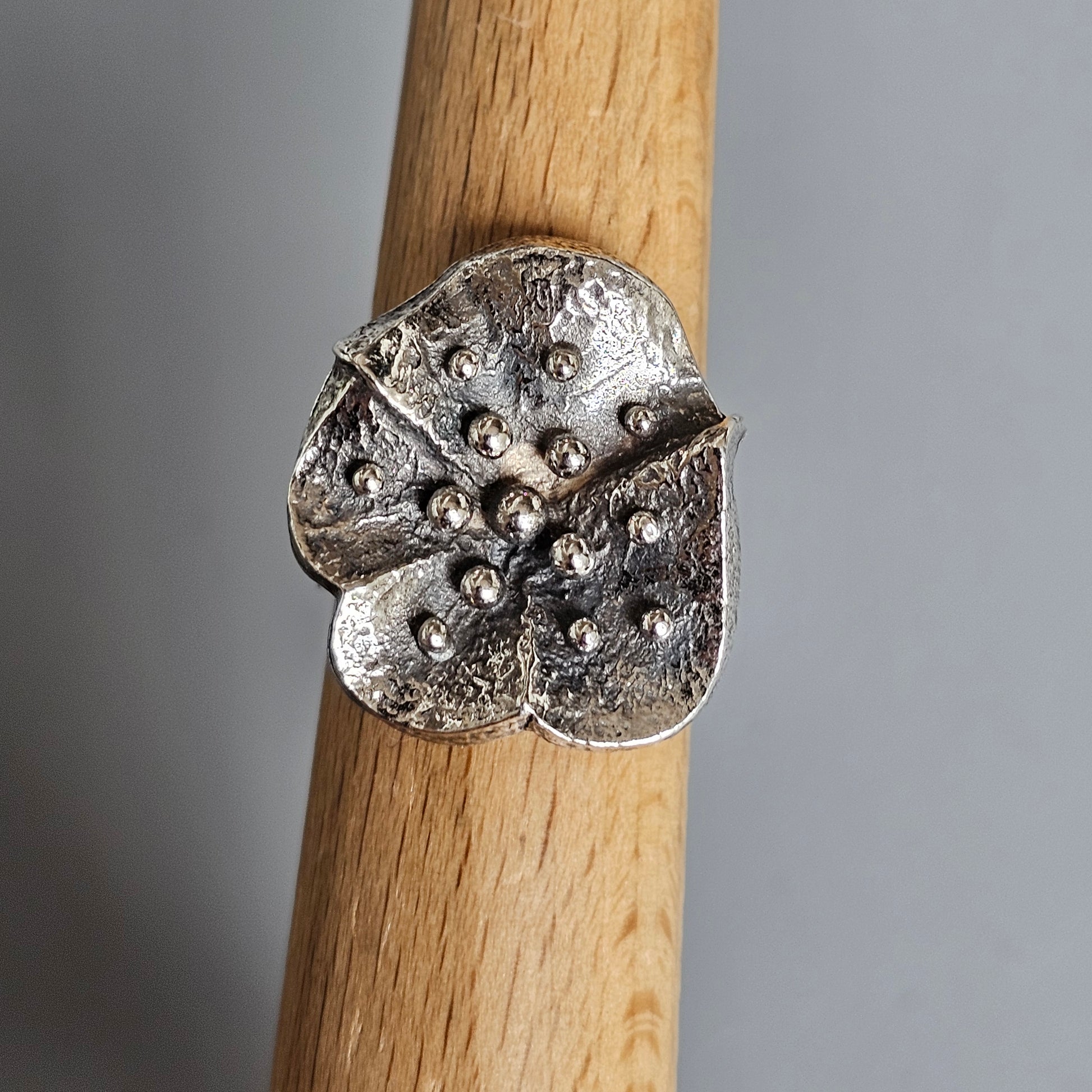 Silver flower-shaped ring with textured petals and small circular indentations.