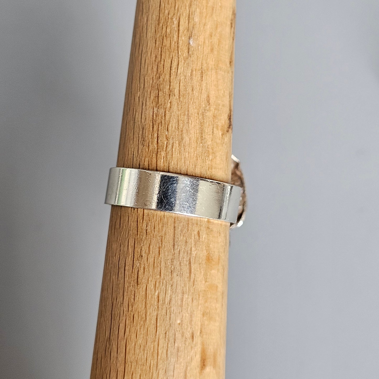 Silver ring wrapped around a wooden dowel or cylindrical piece of wood.