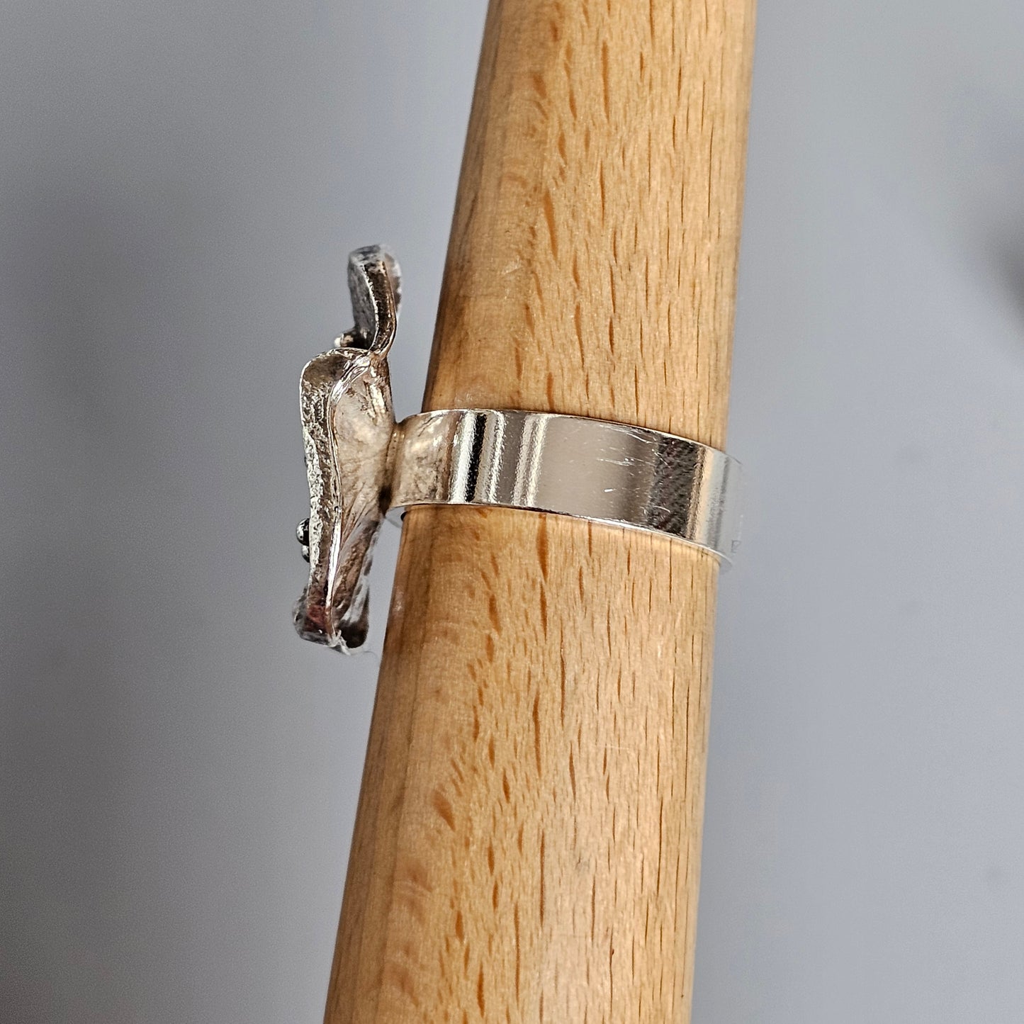 Silver ring featuring a small woodpecker-shaped design on a wooden display stand.