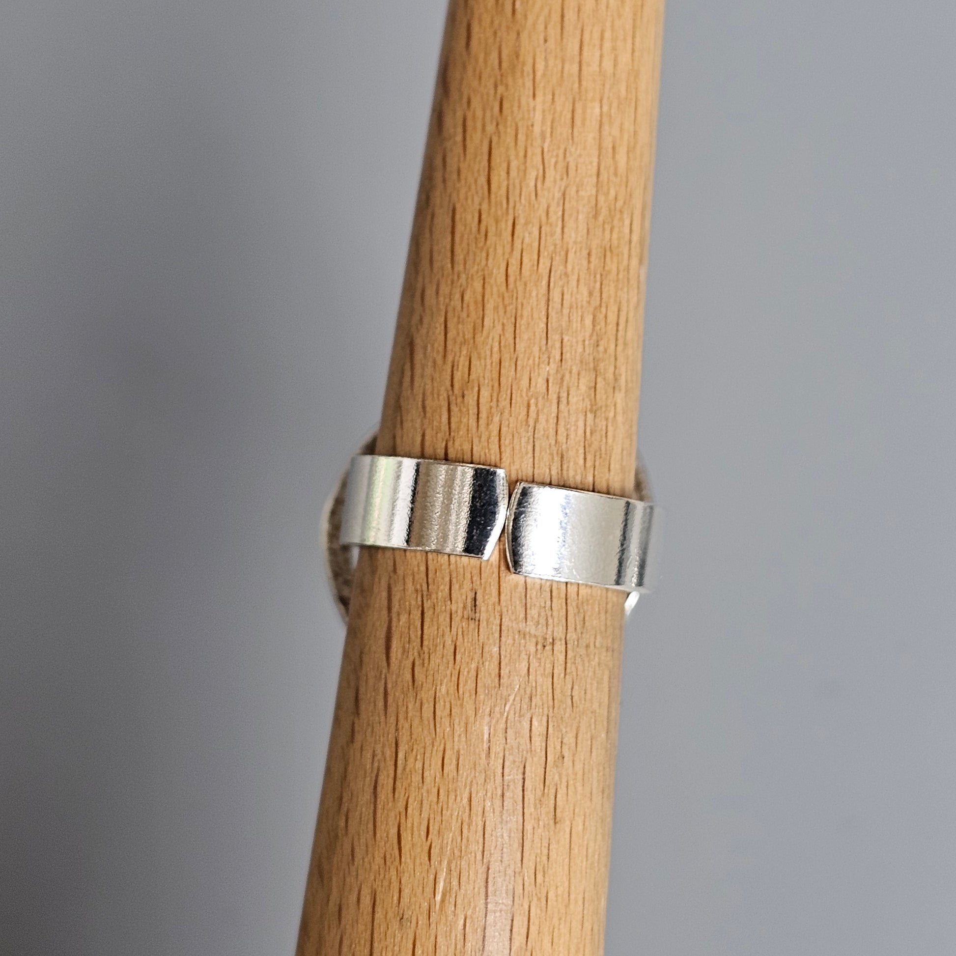 Silver ring with a modern, angular design wrapped around a wooden dowel.