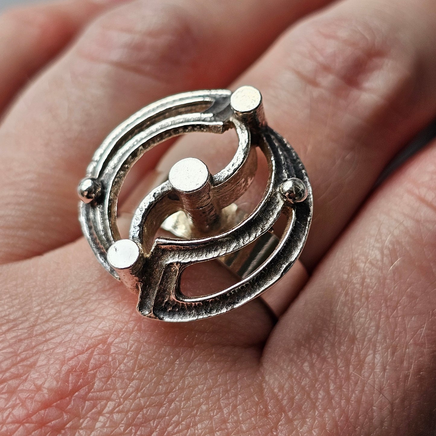 Unique silver ring with an orbital-like design featuring three small circular studs.