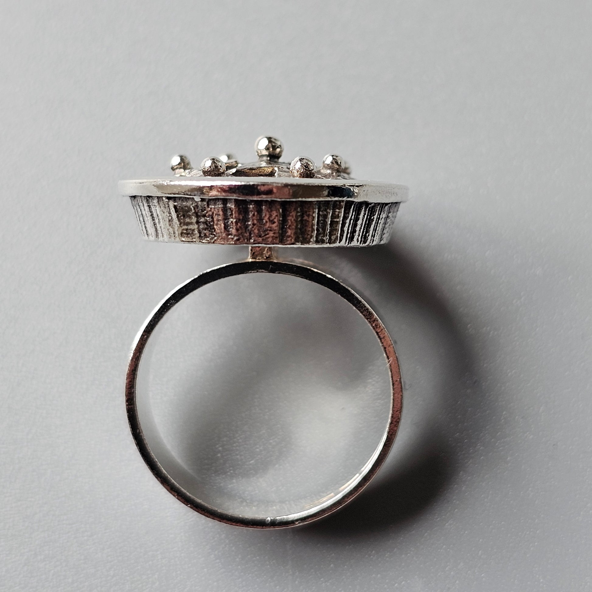 Unique silver ring with a circular platform top adorned with small decorative elements.