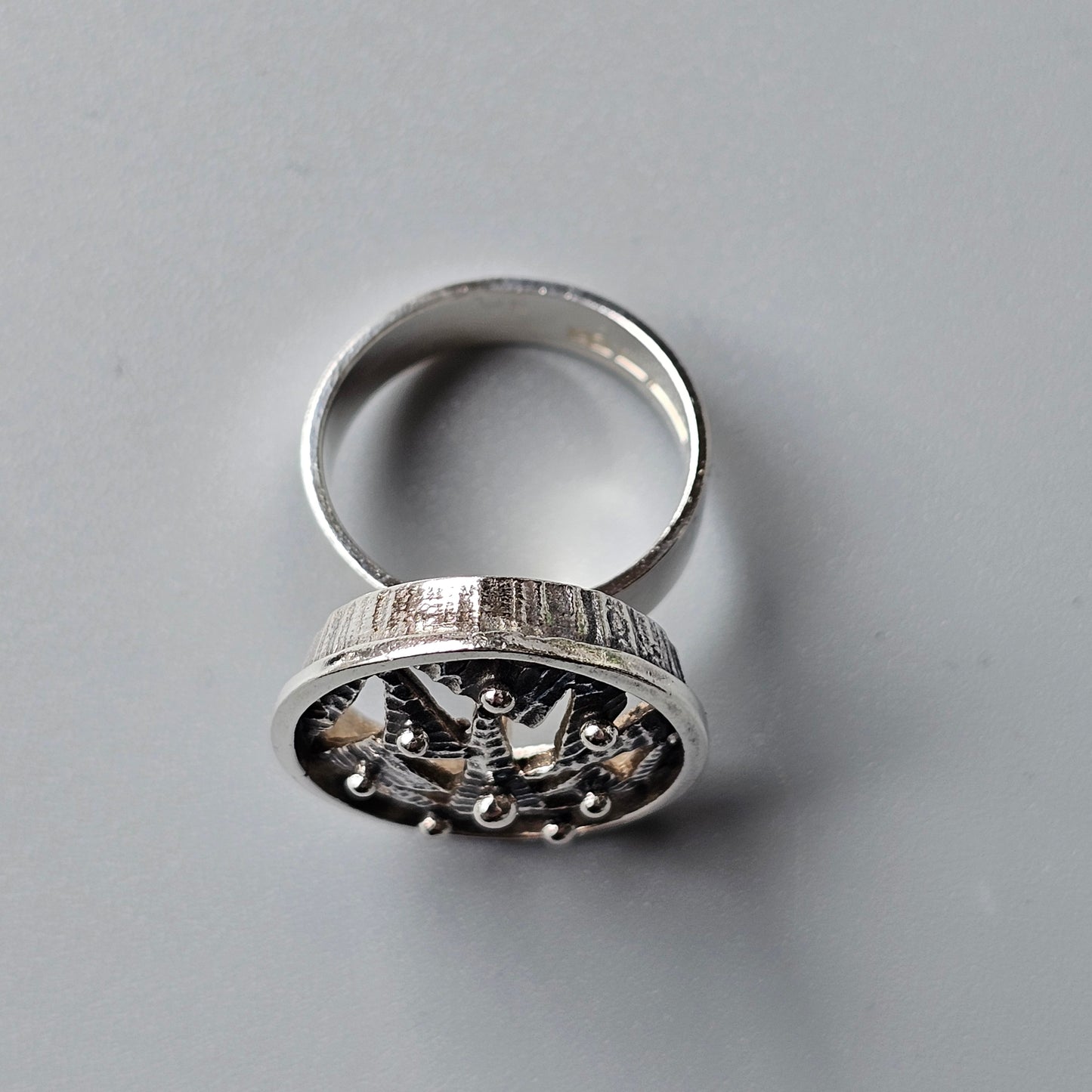 Silver ring with an ornate circular top featuring intricate floral or star-like designs.