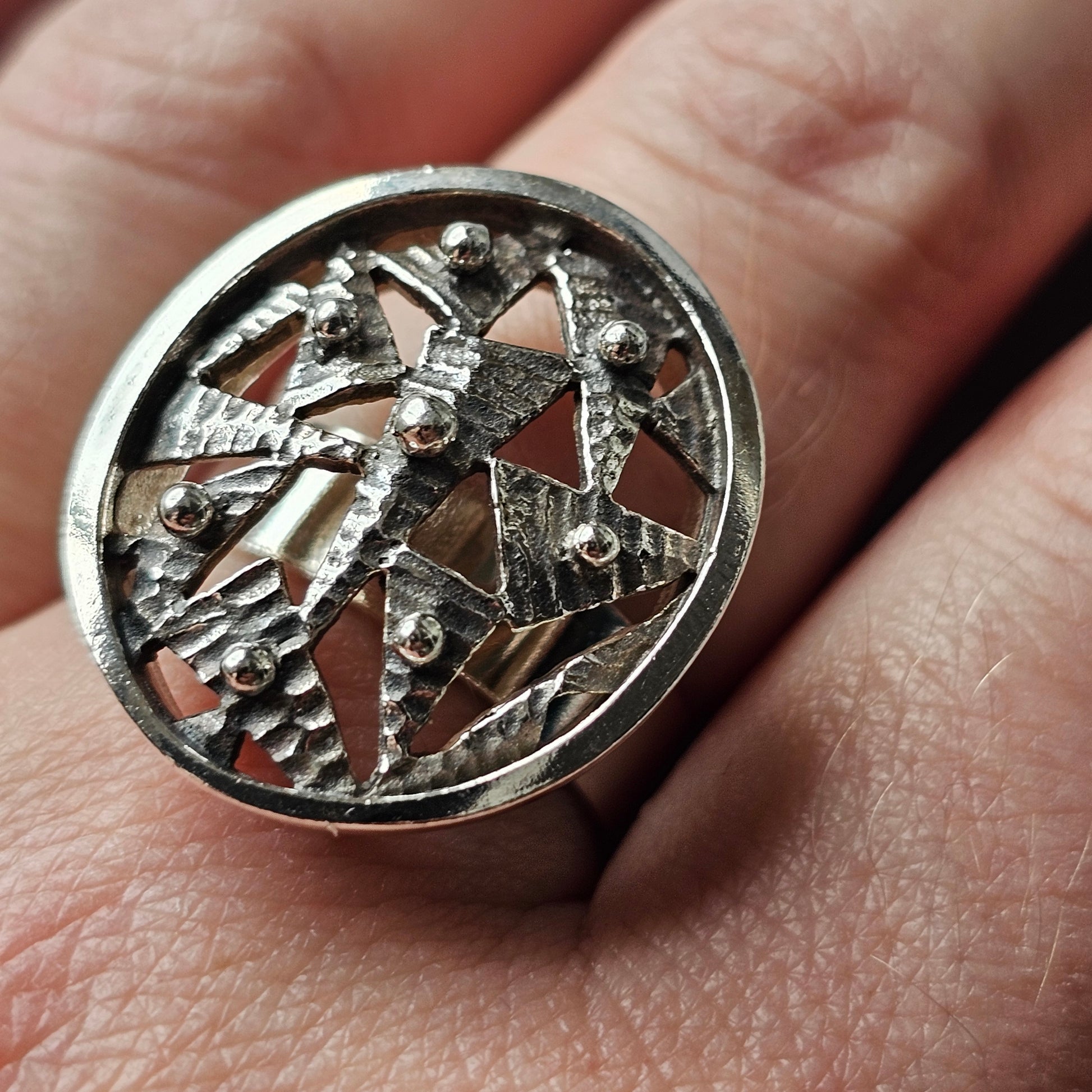 Ornate silver ring featuring an intricate circular design with a figure and geometric shapes.