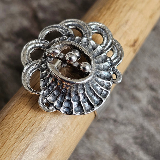 Ornate silver ring with a floral or shell-like design featuring intricate metalwork and small spherical details.