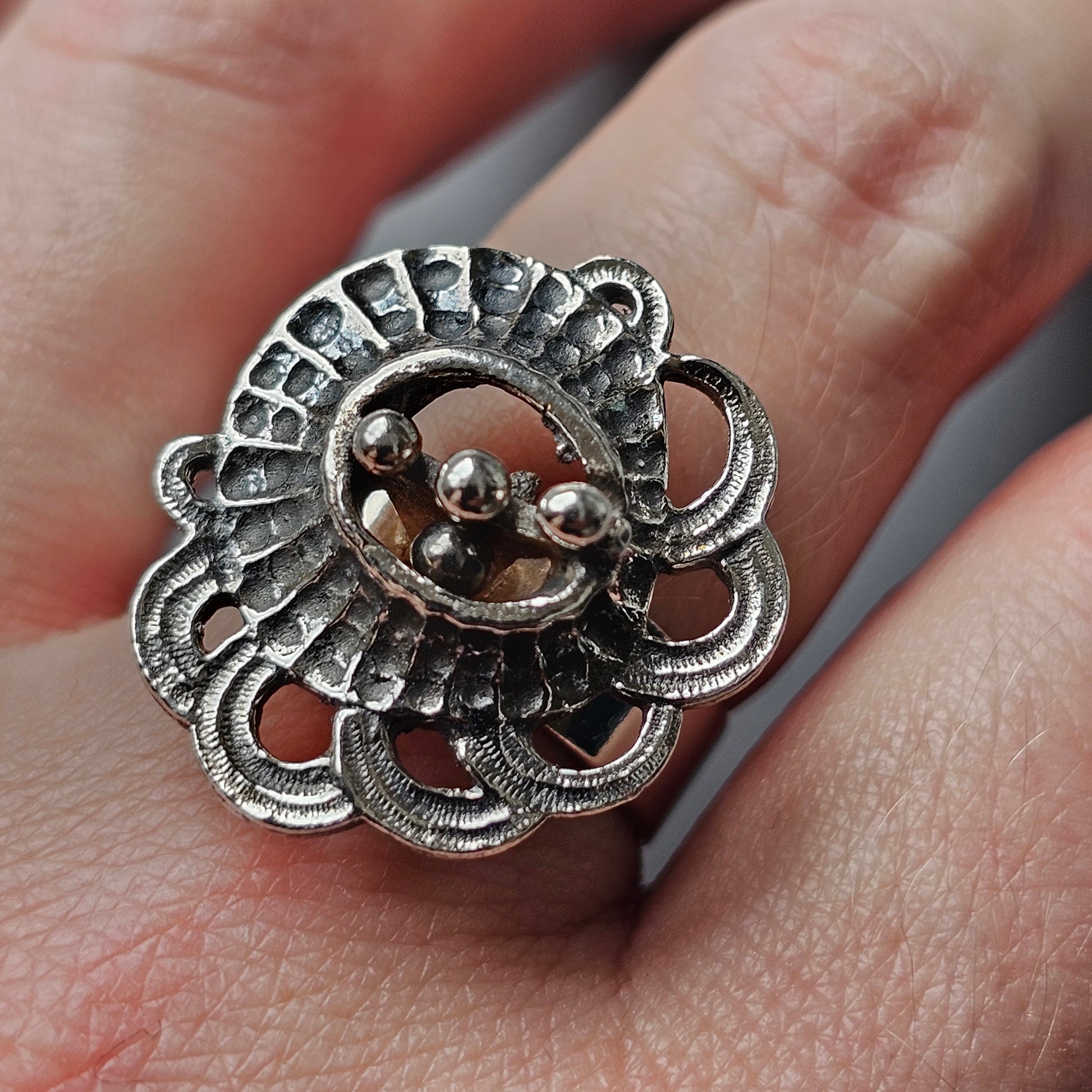 Ornate silver ring with a floral design and small metallic spheres in the center.