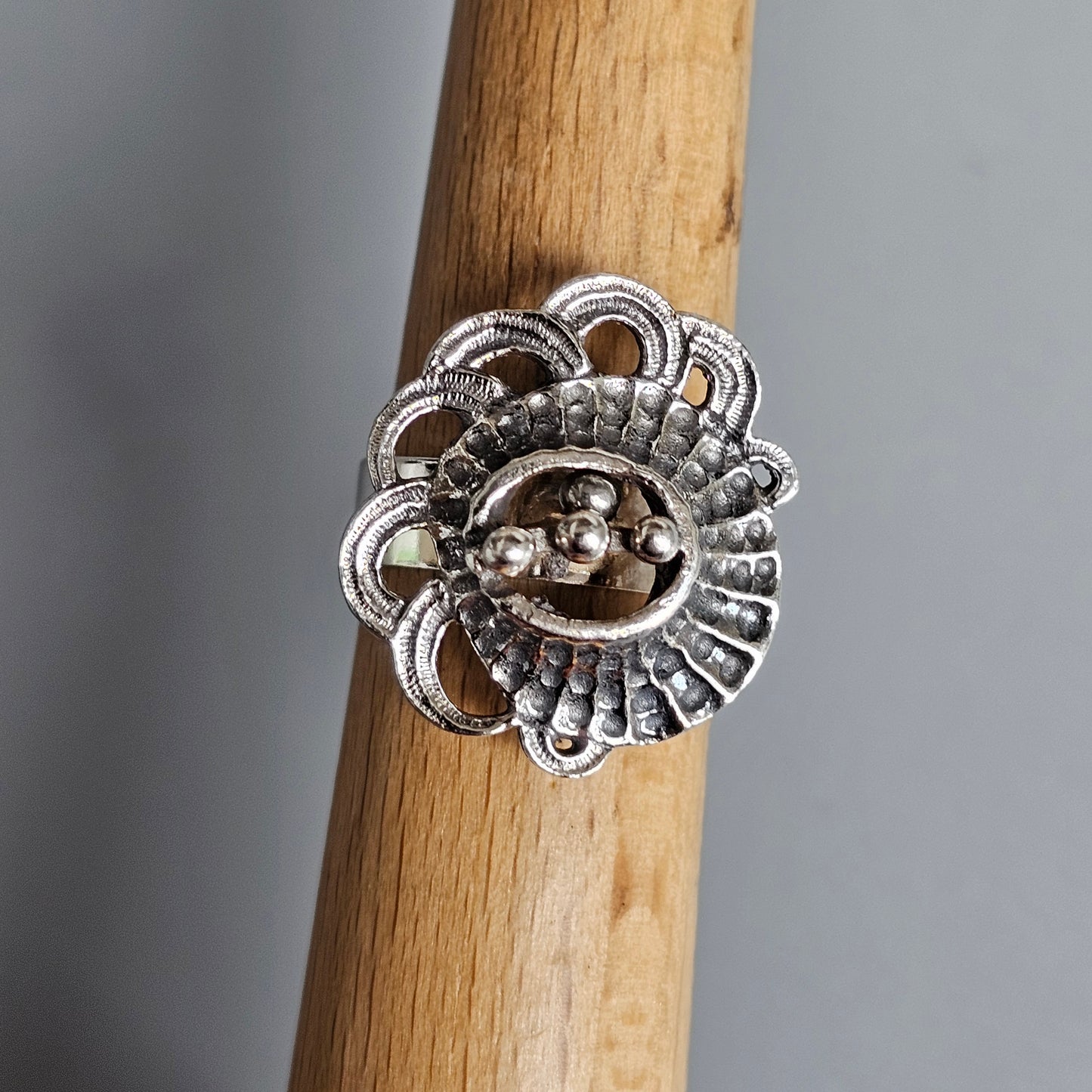 Ornate silver ring with an intricate floral or sunburst design featuring small beads or spheres.