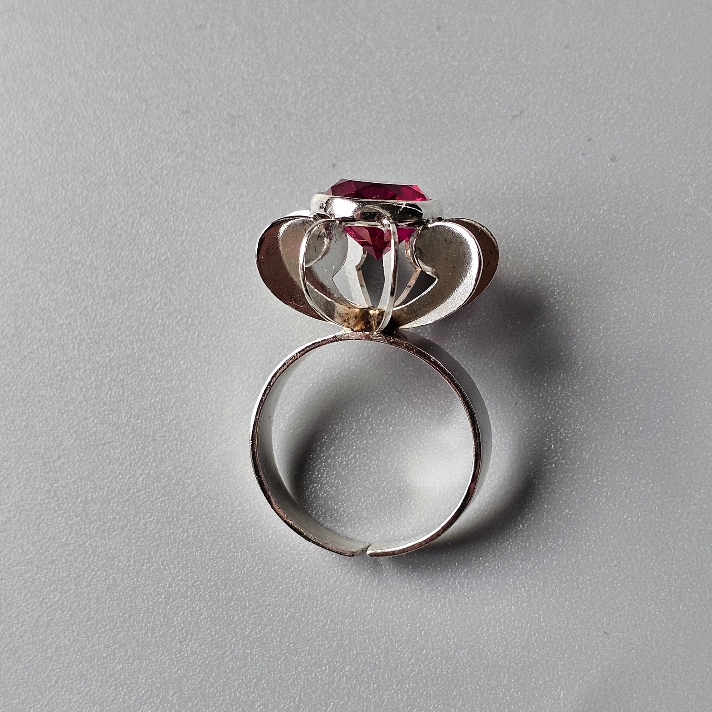 Silver ring with a flower-shaped setting holding a red gemstone.