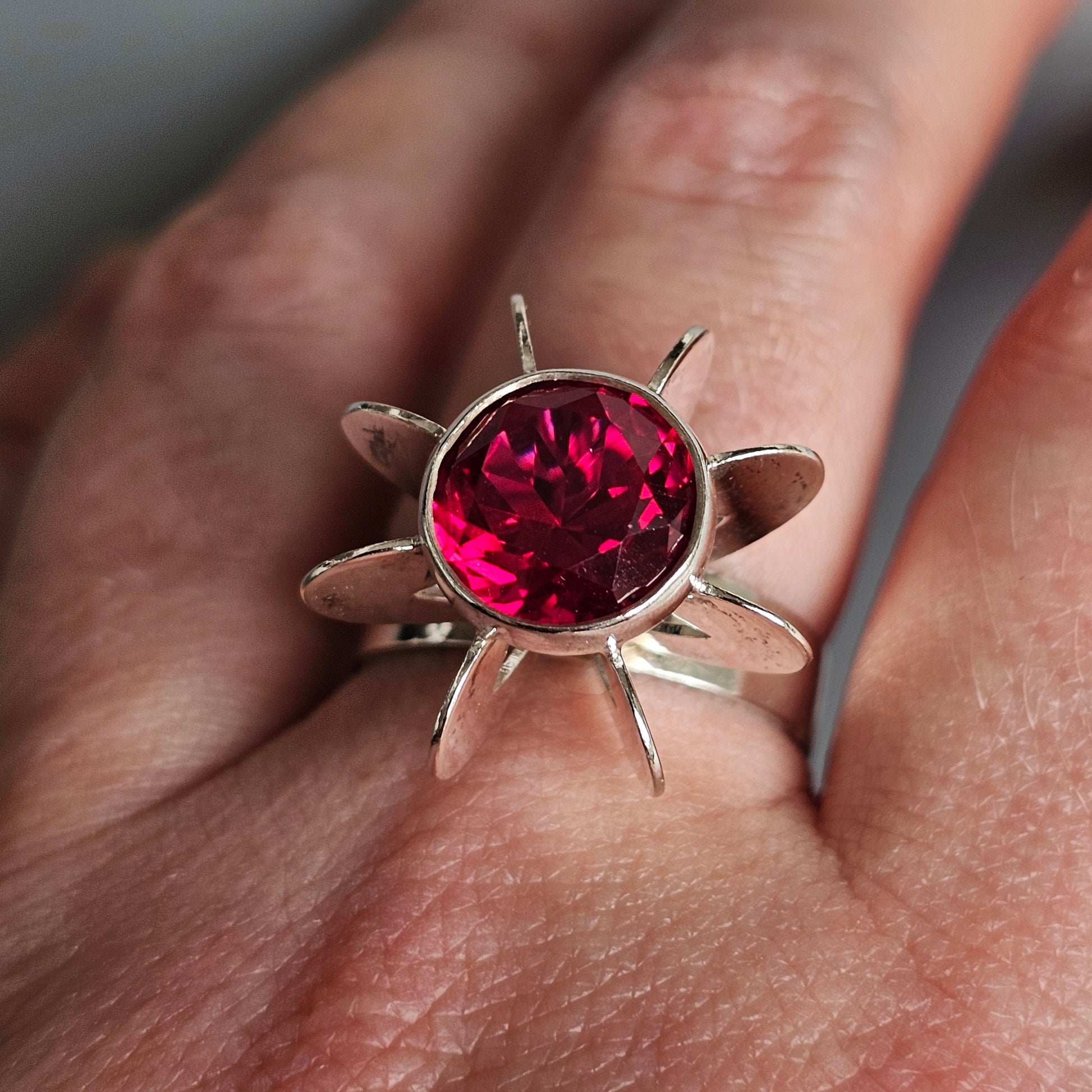 Silver ring with a star-shaped design featuring a round, deep red gemstone at its center.