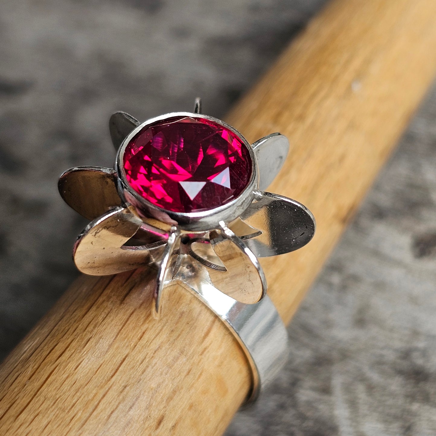 Silver ring with a flower-shaped setting holding a vibrant pink gemstone.