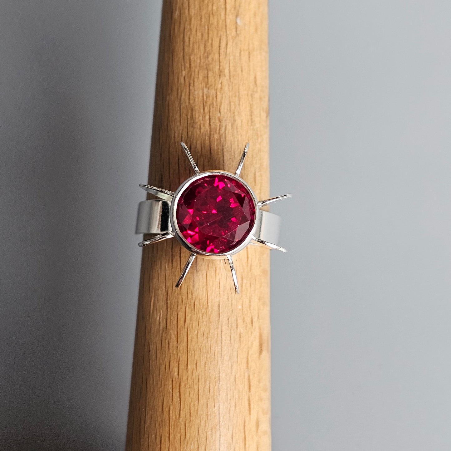 Silver ring with a round red gemstone set in a starburst-like design.