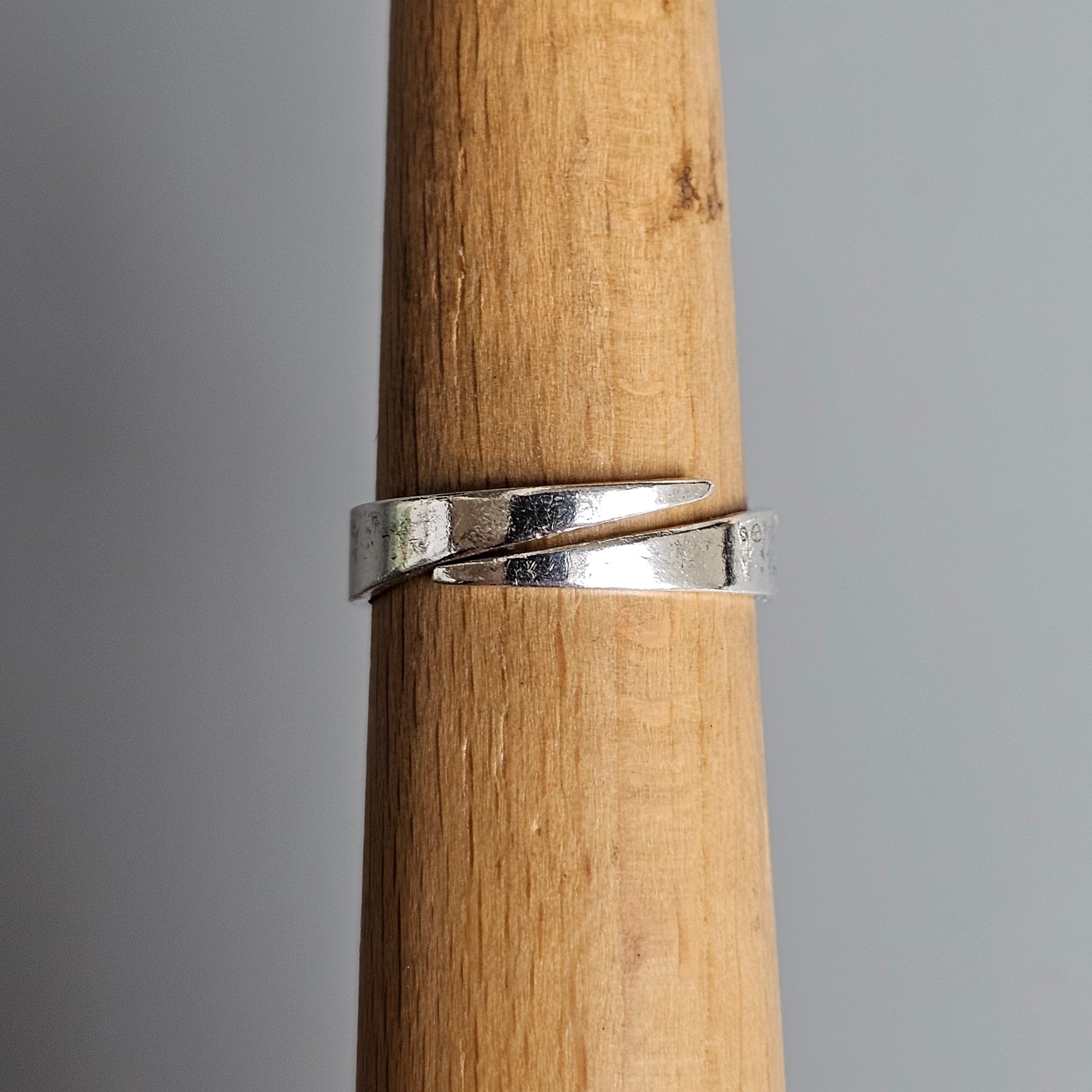 Silver ring with an overlapping, twisted design on a wooden display stand.