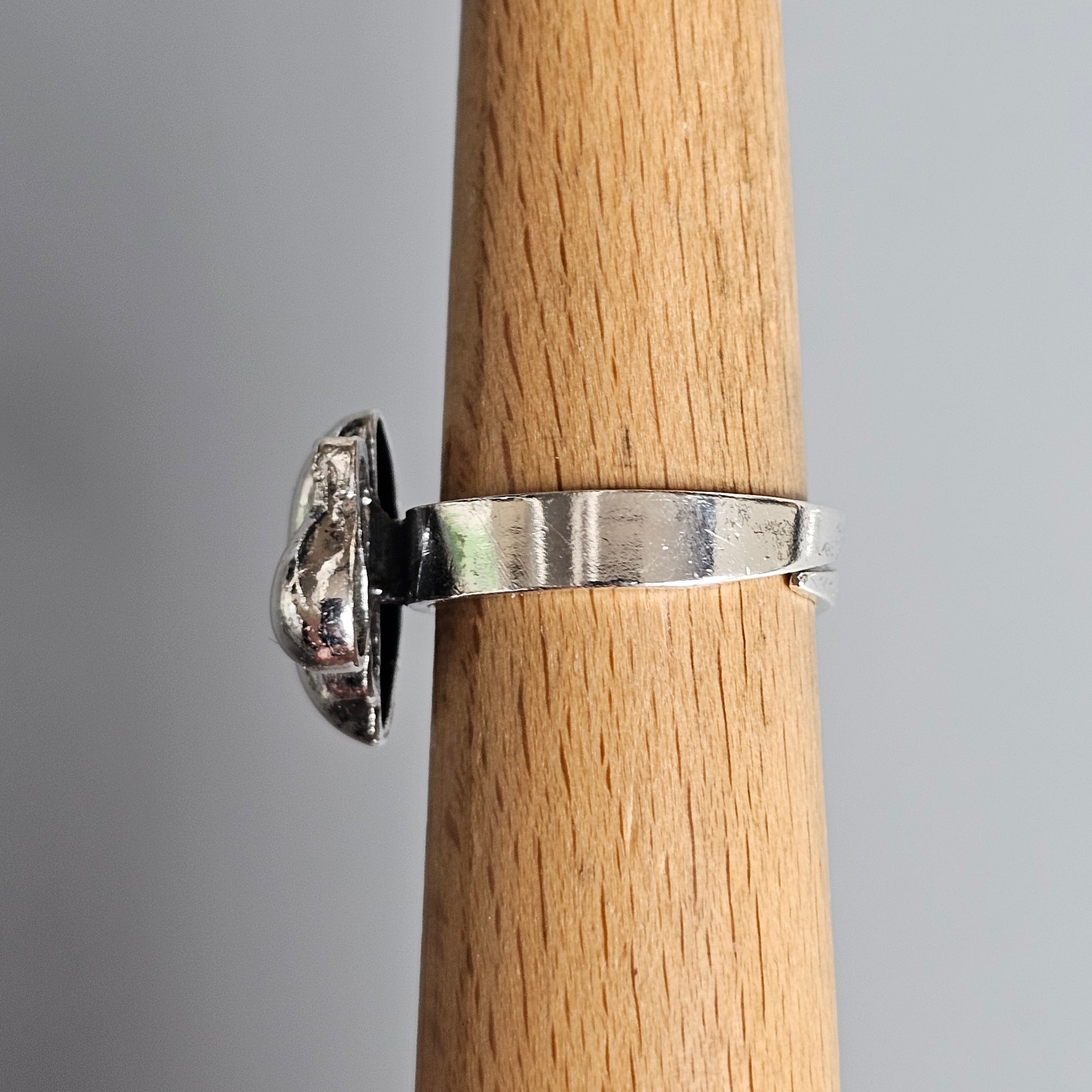 Silver ring with a clear gemstone on a wooden display stand.