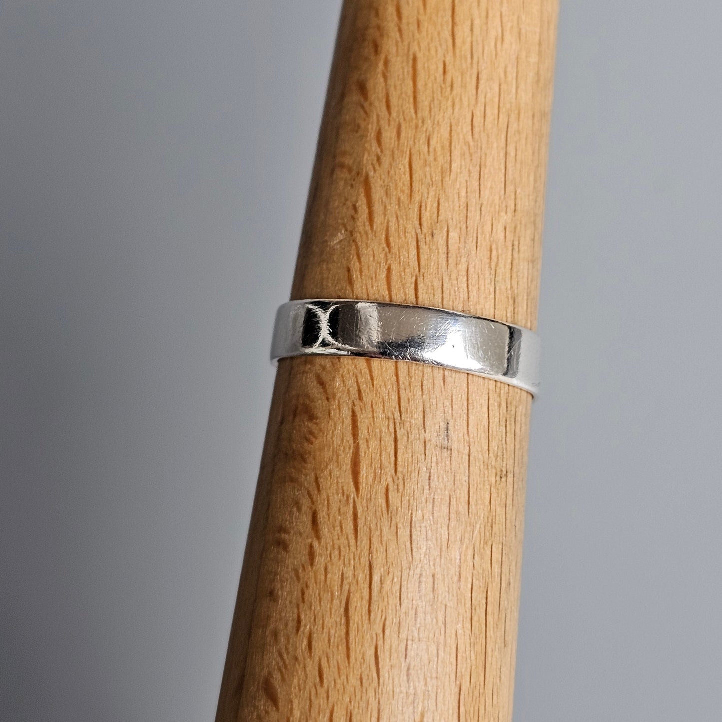 Silver ring with a simple design wrapped around a wooden cylinder.