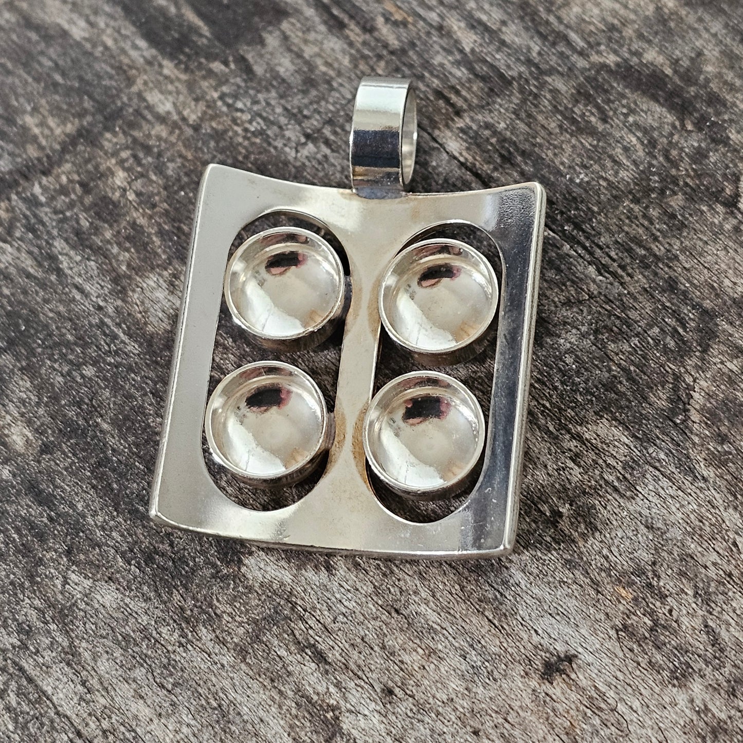 Silver pendant with four circular indentations arranged in a square pattern.