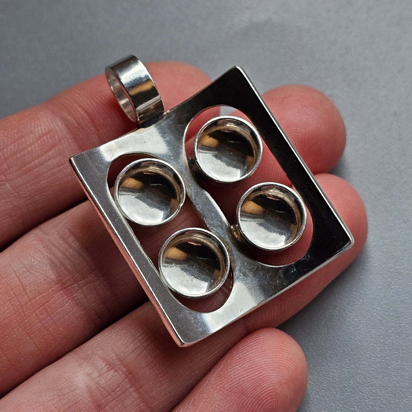 Square silver pendant with four circular indentations arranged in a grid pattern.