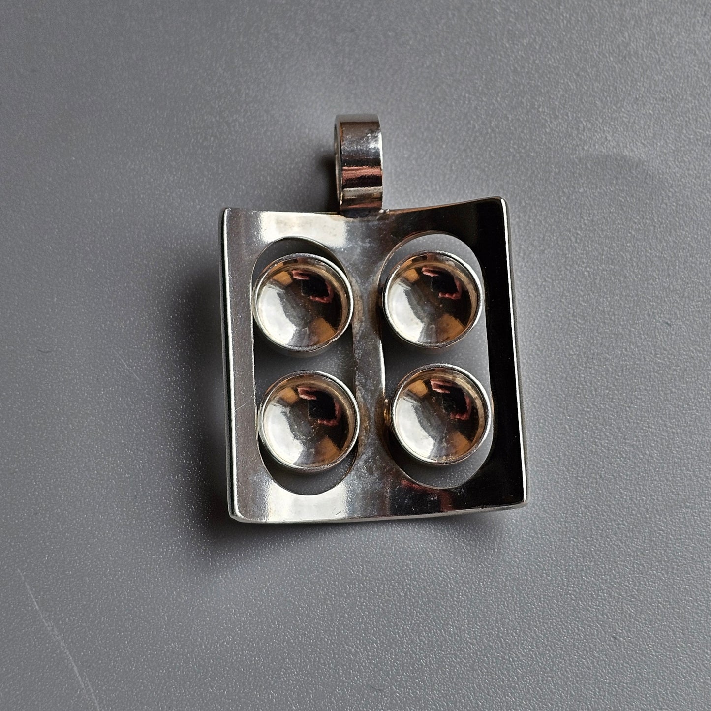 Square silver pendant with four circular indentations.