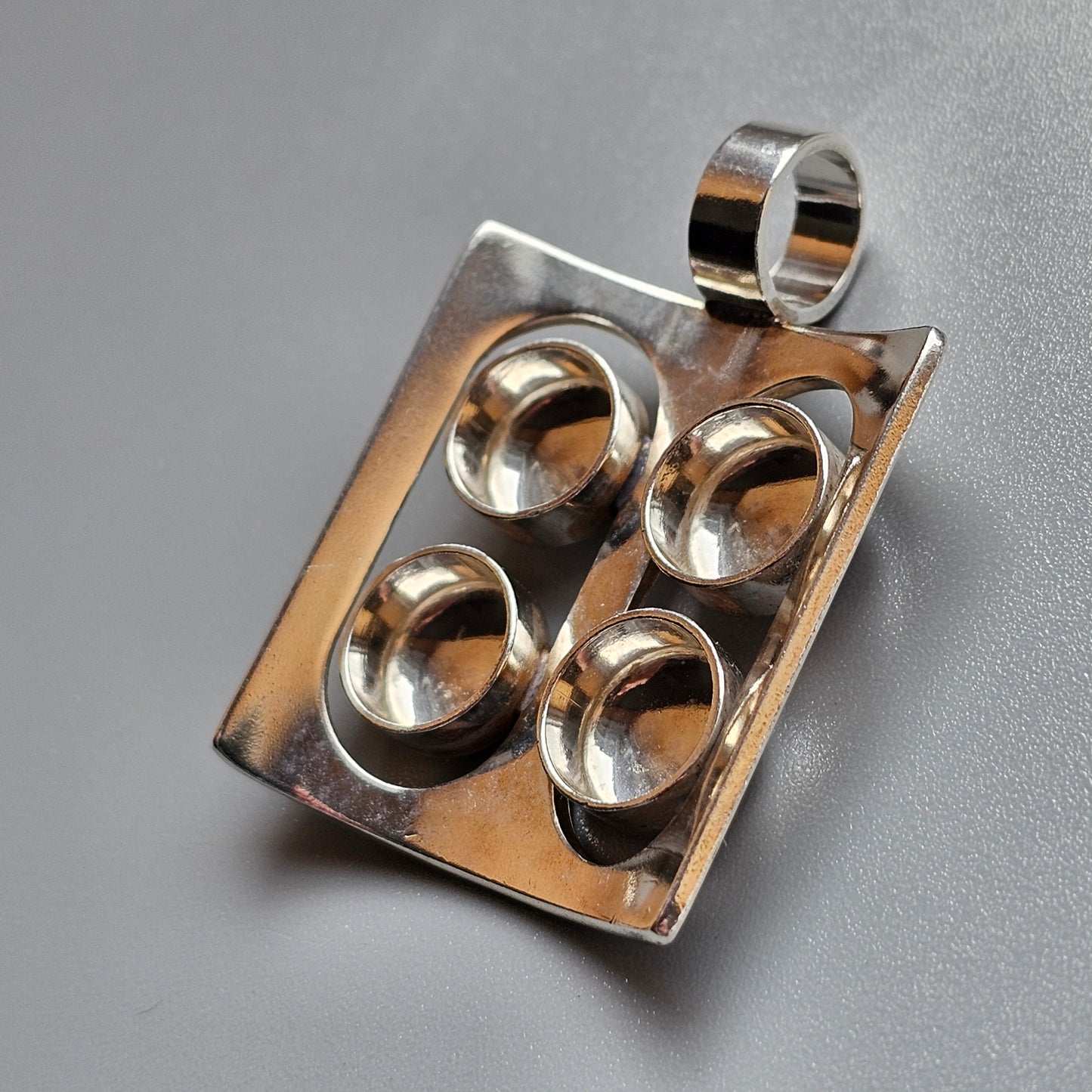 Silver pendant featuring four circular indentations arranged in a rectangular shape.