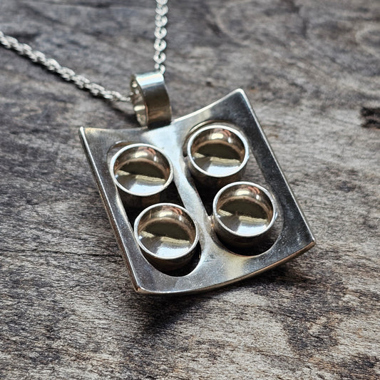 Silver pendant necklace featuring four circular indentations arranged in a square pattern.