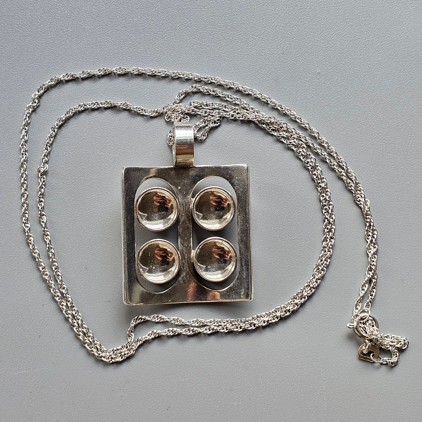 Silver pendant necklace featuring four circular indentations arranged in a square pattern.