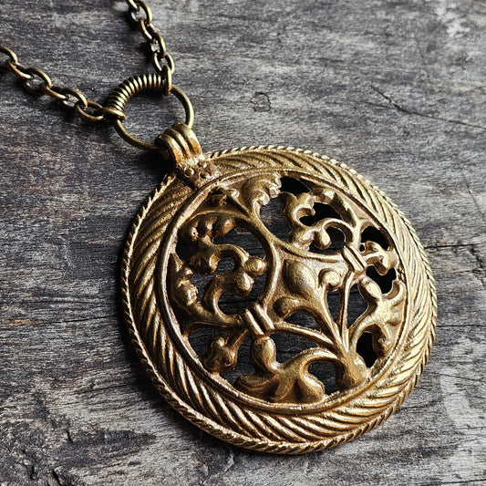 Ornate gold-toned medallion pendant with intricate floral filigree design on a chain.