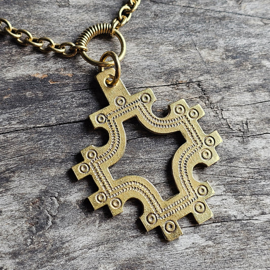 Ornate brass pendant with an intricate, curvy design resembling a stylized cross or floral shape.