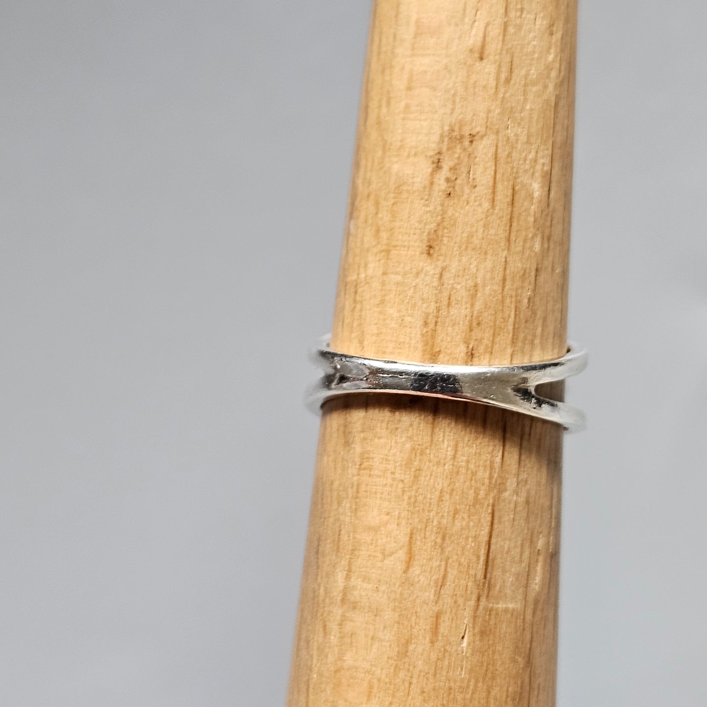 Silver ring with a crossed or X-shaped design worn on a wooden dowel.