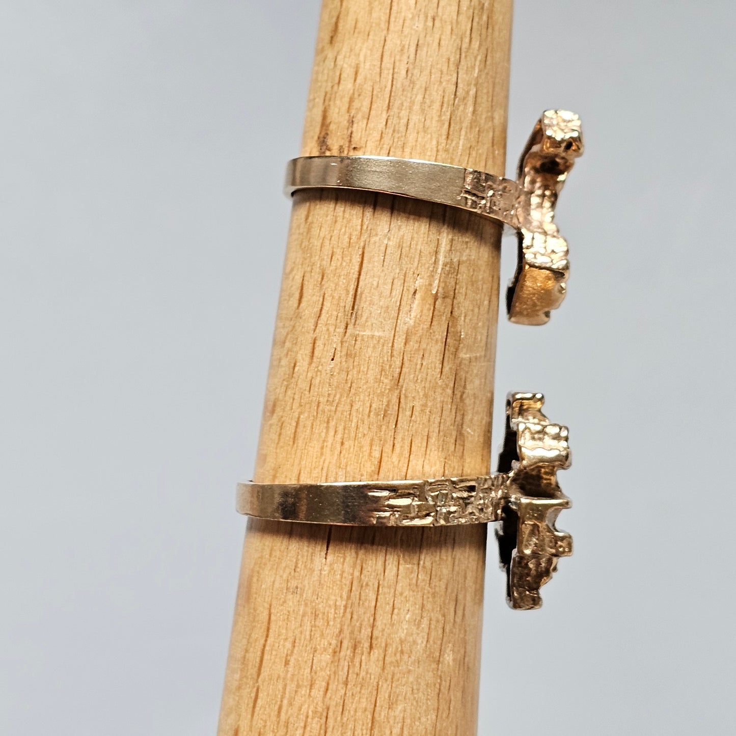 Two gold rings with diamond accents displayed on a wooden stand.