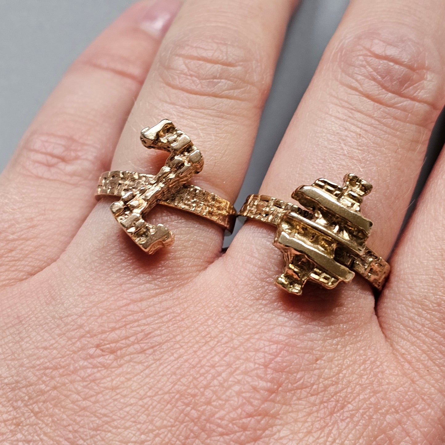 Two ornate gold rings worn on fingers, one shaped like an anchor and the other like a ship’s wheel.