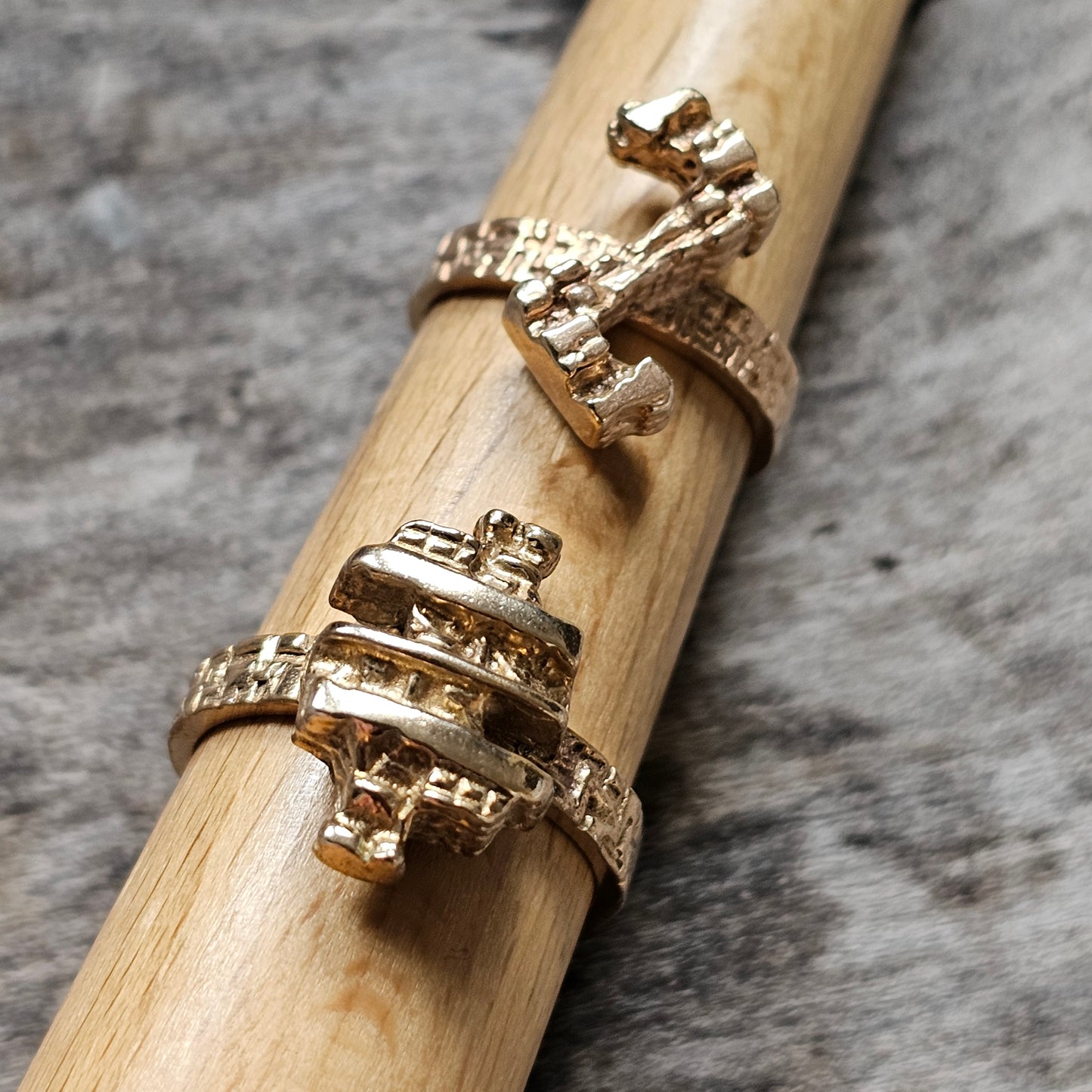 Two gold rings with intricate designs on a wooden dowel.