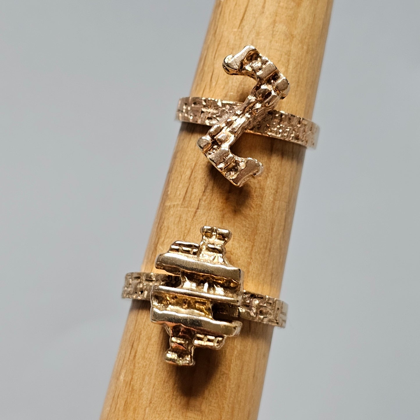 Two gold rings with geometric designs displayed on a wooden surface.