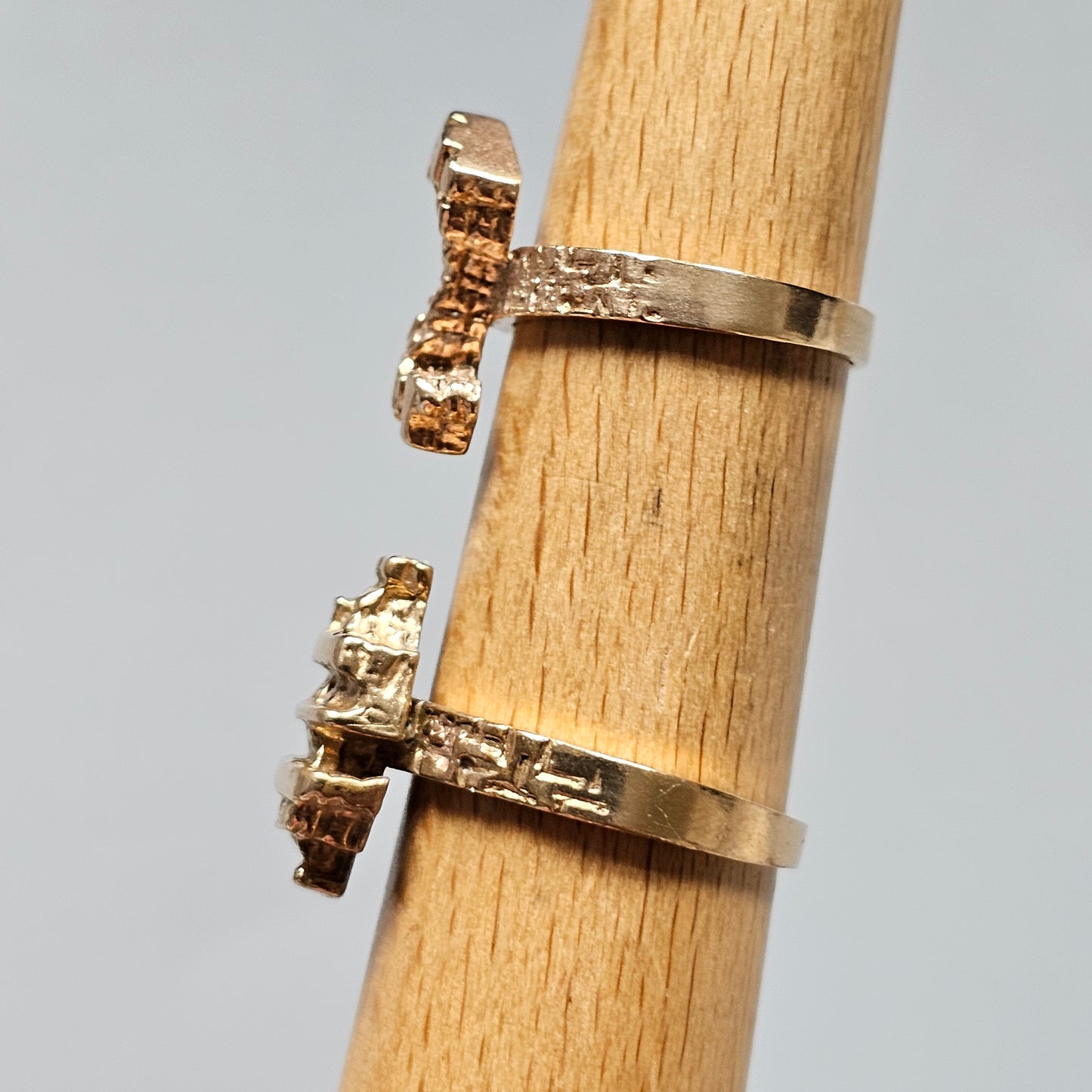 Two gold rings with protruding gemstone settings on a wooden cylinder.