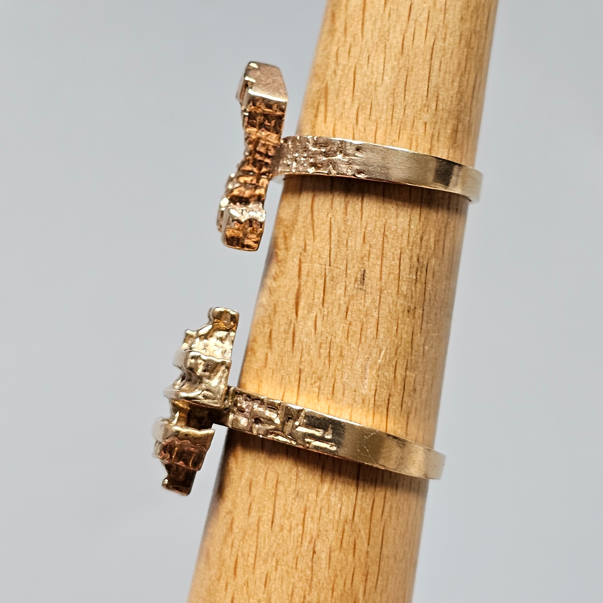 Two gold rings with protruding gemstone settings on a wooden cylinder.