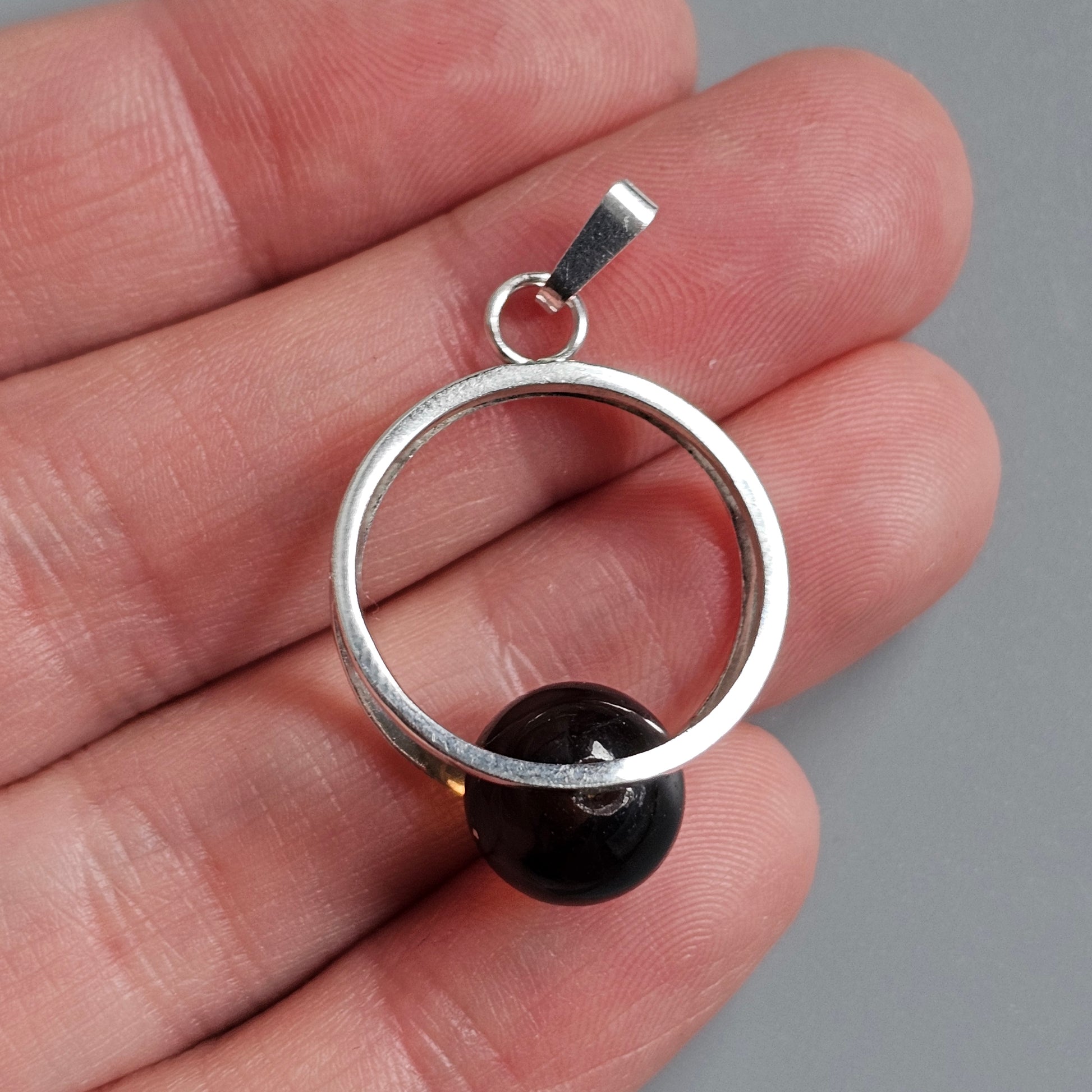 Silver circular pendant with a black bead or sphere attached.