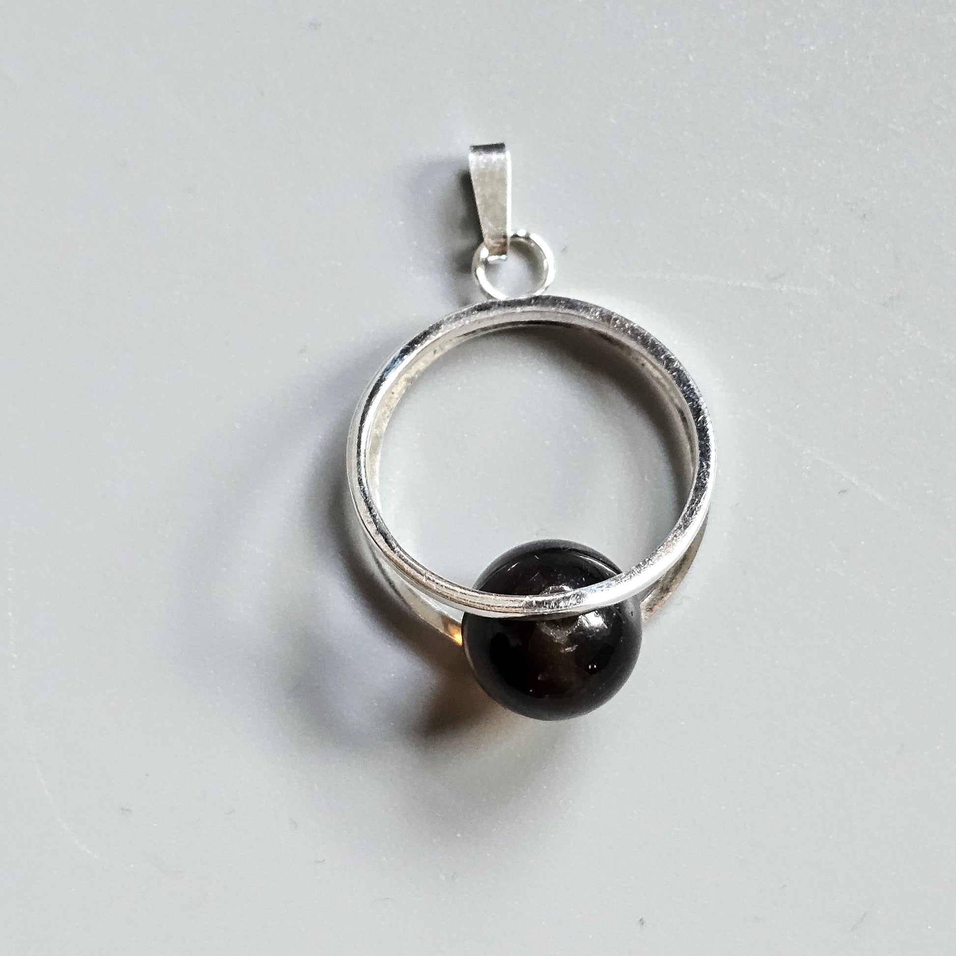 Silver pendant featuring a circular design with a dark spherical bead.