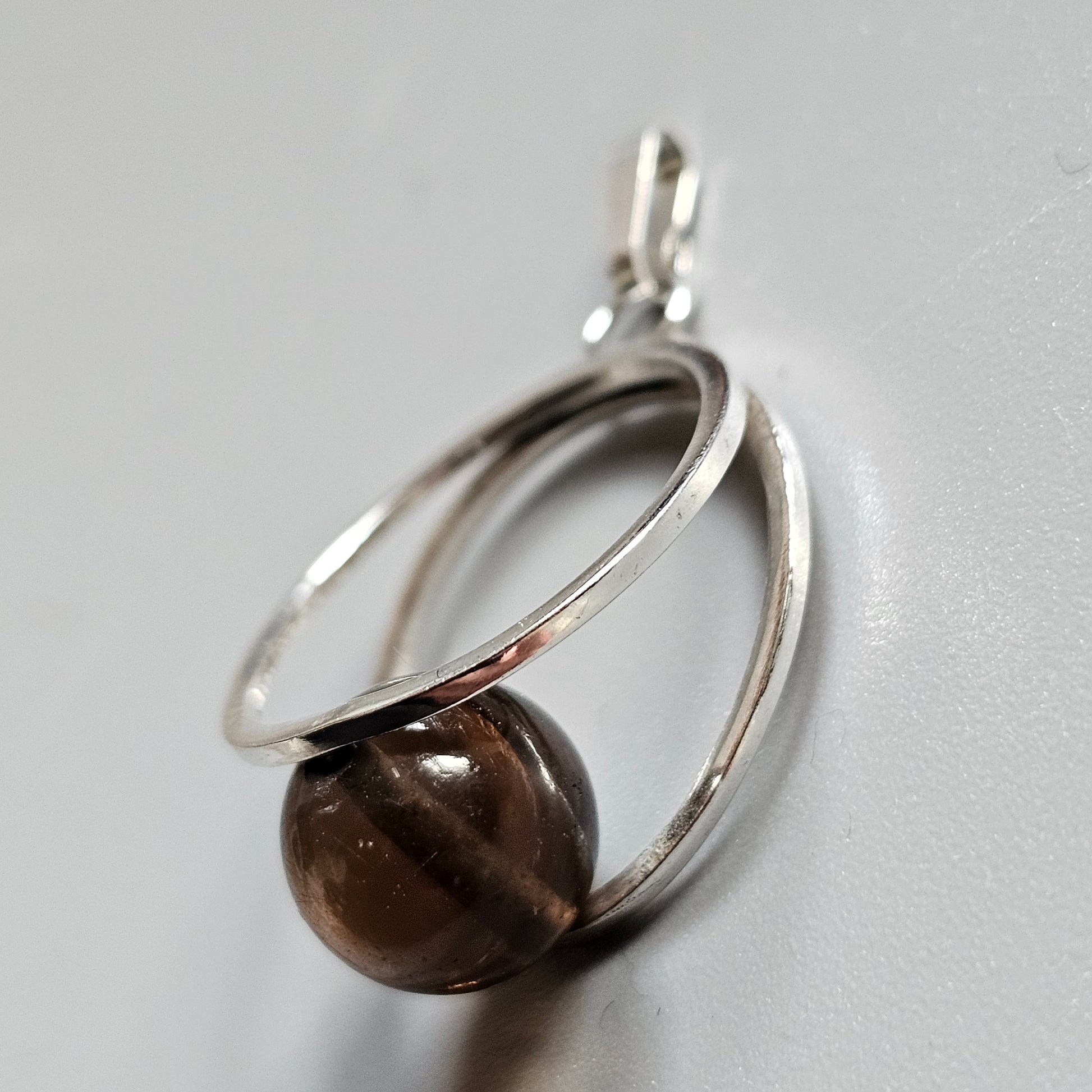 Silver pendant featuring a dark brown spherical bead encircled by curved metal loops.